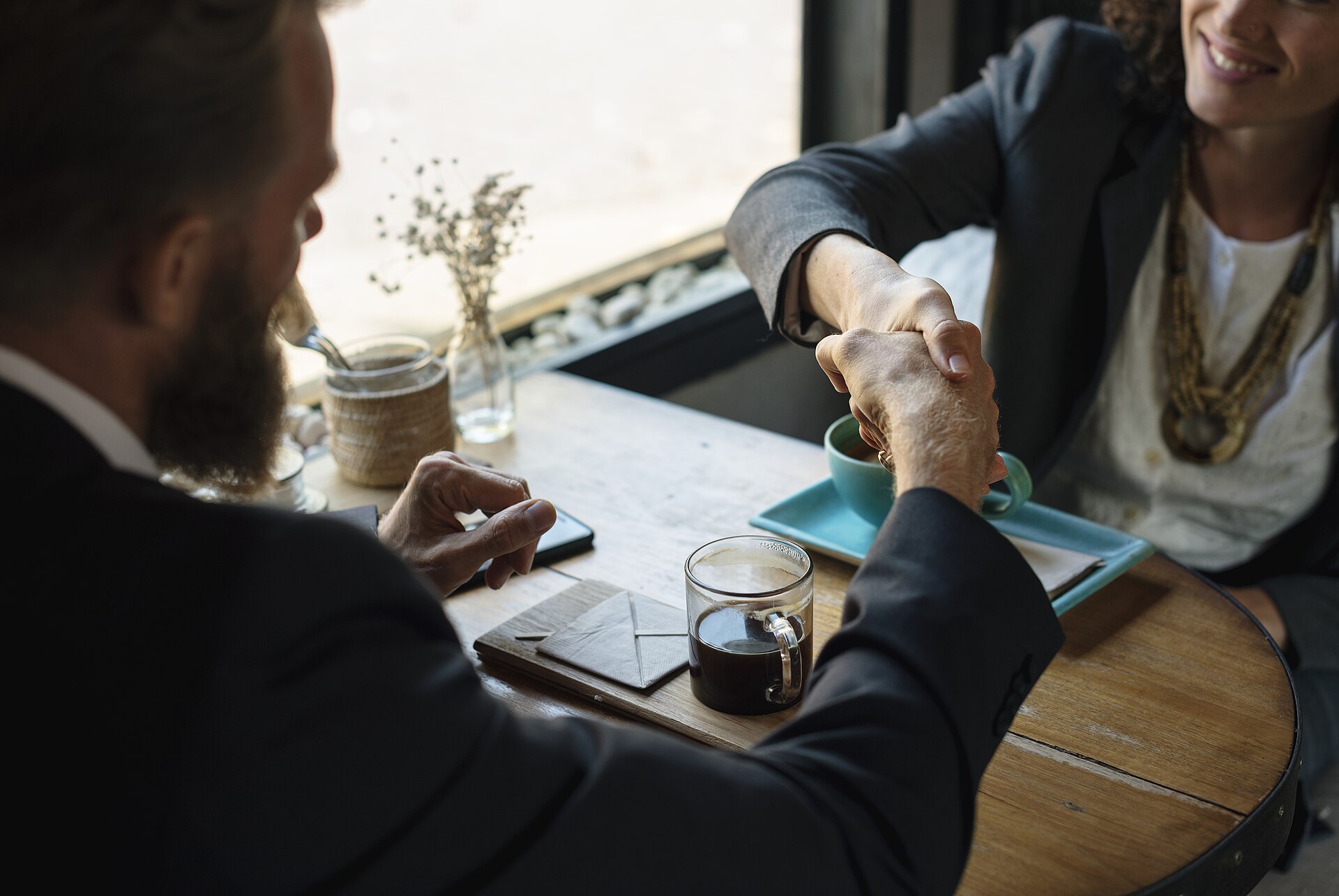 Two people shaking hands in agreement at a coffee shop